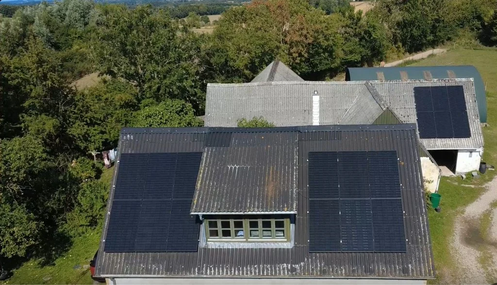 Dronefoto af landejendom med sorte solcellepaneler på begge sider af kvisten