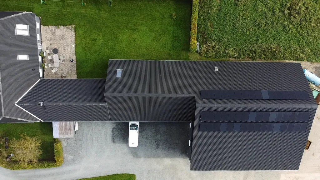 Dronefoto af sort bygning med striber af solcellepaneler på ståltaget