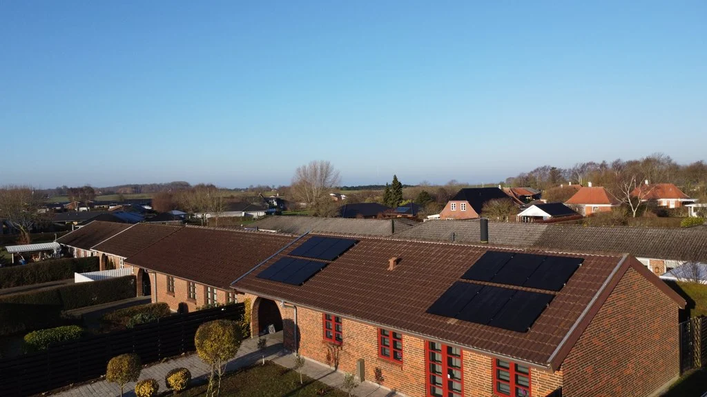 Dronefoto af rødstenshus med sorte solcellepaneler på begge tagflader